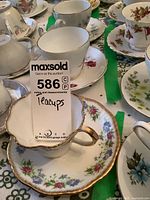 Close-up of white teacup and saucer with blue and pink floral design and gold trim edged scalloped saucer