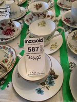 Overview photo showing multiple china teacups and saucers on a table, highlighting floral patterns and gold rims.