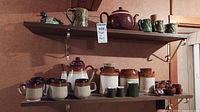 Full view of ceramic teapot, mugs, canisters, jugs and small containers arranged on two shelves