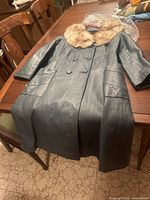 Full view of the vintage black leather coat laid flat on a table showing front double-breasted buttons and pockets.