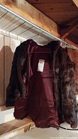 Photo showing the vintage mink fur cape hanging on a metal rod in a basement with wooden walls and ceiling.