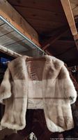 Front view of the vintage mink stole hanging on a metal rod showing the short sleeves and light beige fur.