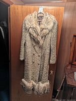 Front view of the vintage Persian lamb fur coat hanging on door showing the fox fur collar and hem.