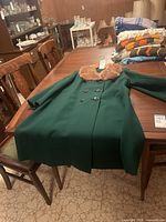 Green vintage wool coat with mink collar displayed on table with folded blankets in background.