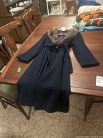 Full view of vintage dark wool coat laid out on a table, showing length and belt.