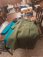 Two vintage wool coats laid on a wooden table with folded knitwear in background. One green coat with pink mink collar over the teal coat with dark collar.