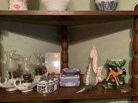 Shelf showing four genie style oil lamps, Wedgwood jasperware boxes and vase, Mary with children figurine, and metal trinket boxes.