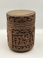 Close-up of the taller cylindrical box showing intricate openwork carving of figures and foliage.