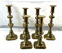 Wide view of all six antique brass push-up candlestick holders arranged in groups by height.