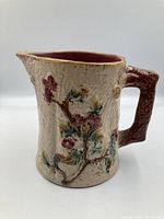 Side angle showing floral relief design, handle, and spout of the Majolica pitcher