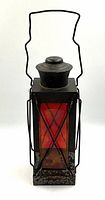 Front full view of antique red glass signal lantern with metal frame and handle, showing overall shape and structure.
