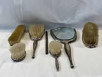 Overview of all vanity set components: hand mirror, four sterling silver handled brushes, monogrammed cream handle brush and metal file