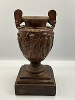 Front view of urn showing relief figures and scroll handles