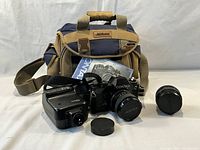 Overall view showing camera body with mounted lens, flash unit, two lenses with caps, charger, and Nikon bag in background
