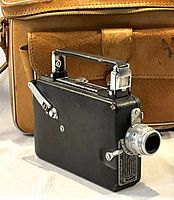 Close-up photo of the Kodak cine movie camera with black body and silver lens in front of the leather bag.