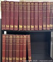 Two-tier shelf display of burgundy cloth-bound volumes I–XI (top row) and XII–XXII (bottom row), showing gilt spine titles and medallions
