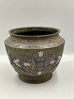 Front view of champlevé jardiniere showing colorful floral and leaf enamel design with geometric patterned rim.