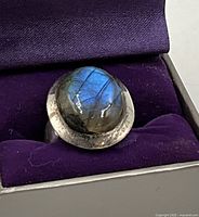 Top angled view of the sterling silver cocktail ring showing the blue flashes of the oval labradorite cabochon stone in the bezel setting, on a purple velvet background.