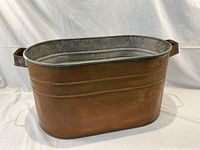 Oval copper tub showing copper exterior with horizontal bands and attached metal handles.