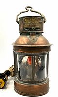 Front view of vintage copper masthead lantern showing clear glass panels, metal frame, electrical bulb inside and electrical cord with plug.