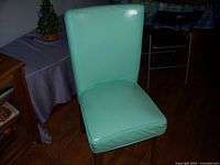 Front view of blue leather-like upholstered chair with cushioned seat and backrest, next to wooden table and in a room with wood flooring
