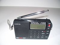 Front view of black CCrane Mini SWP radio with digital display showing frequency 8.59, extendable antenna extended, control buttons and power button visible.