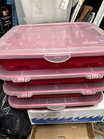 Four stacked plastic storage bins with clear lids, red bases with round compartments visible inside to store Christmas bulbs.
