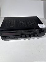 Front and top view of black Denon stereo receiver showing multiple control knobs and ventilation grilles.