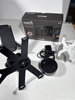 Photo showing Notifi smart wireless doorbell box, power adapter, and multiple mounting accessories including black plastic brackets and white adjustable holder.