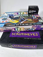 Three board games displayed: The Game of Life Twists & Turns, ScrutinEyes, and Cinelinx Deluxe Edition with game components and boxes.