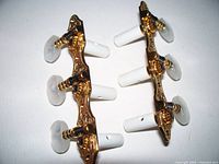 Front view showing two gold plated classical guitar tuner plates each with three white tuning pegs and pearlescent white tuning keys attached.