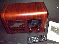 Front perspective of the Grace Victoria radio system and remote control showing wood finish, speaker grille, digital display, and control knobs.