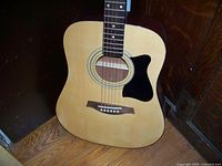 Front view of the full acoustic guitar showing the natural wood top and black pickguard