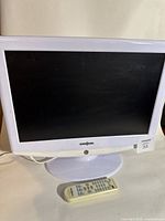 Front view of white Insignia 19 inch LED TV with remote placed in front on white stand.