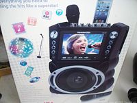 Photo of the Karaoke USA karaoke machine box displaying the unit with two microphones and LCD screen showing a female singer.