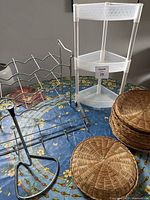 Photo showing stacked wicker baskets, white corner shelving unit, and various metal racks on a floral tablecloth.