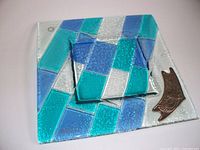 Top view of glass tray and smaller matching piece showing patchwork of blue, turquoise, and clear glass with silver bird accent