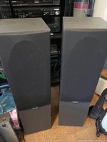 Front view of two black Polk Audio floor standing speakers with black fabric grille covering the driver area.