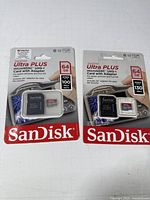 Two packages of SanDisk Ultra Plus 64GB microSDXC cards with SD adapters, sealed retail packaging showing specifications and branding.