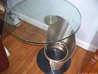 Full view of the art glass table showing circular glass top and stainless steel curved base on wooden floor.