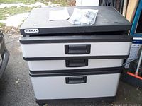 Front view of Stanley tool box storage cabinet with three drawers and black handles, black top surface, and light gray drawers.