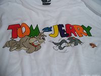 Close-up of front T-shirt print showing colorful Tom, Jerry, and Spike characters with logo text