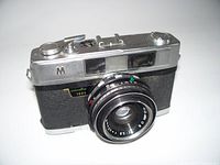 Image showing front and lens of Minolta 1000 rangefinder camera, detailing the silver metal and black textured body with visible minor wear.