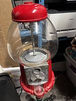 Full view of red topped glass globe vintage style candy gumball machine with silver coin mechanism.