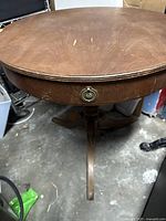 Close-up of the round wooden tabletop with drawer and round metal pull, showing surface wear and scratches.