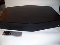 Black ZVOX TV speaker with fabric grille and included silver remote control in front on white background.