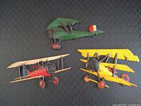 Top view of three vintage cast aluminum WW1 era biplane decorative airplanes in green, yellow, and red with minor paint chips.