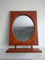 Front view of rectangular teak frame with inset circular mirror and shelf below