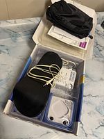 Overview of Dr. Ho's massager device including cords, electrode pads in packaging, black pouch, all placed inside original box on countertop.