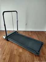 Full view of the Qslim folding treadmill on wooden floor, showing the folded handlebars and running belt.